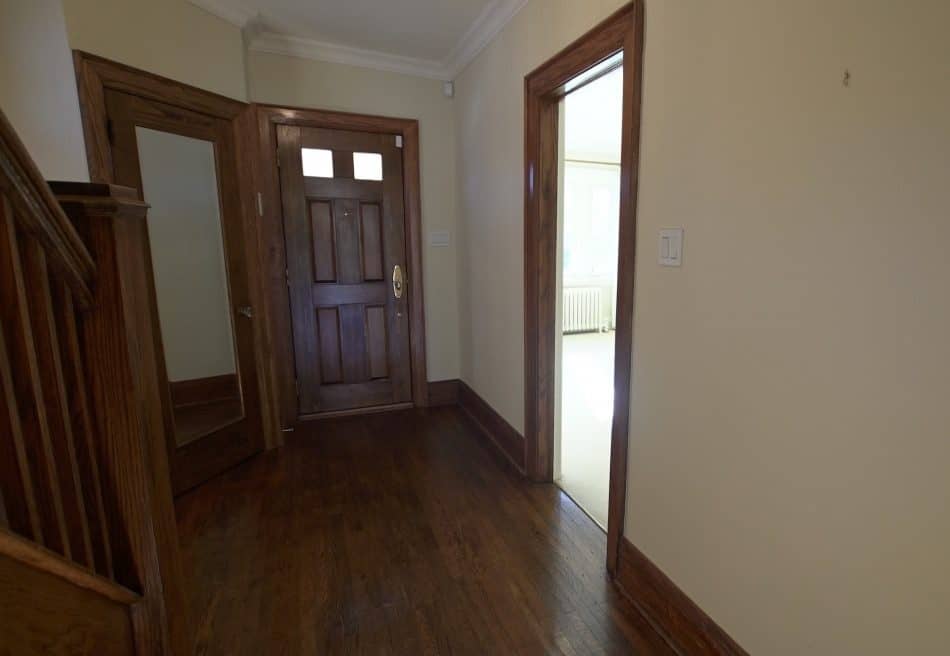 A narrow hallway with hardwood floors, white walls, and a visible staircase