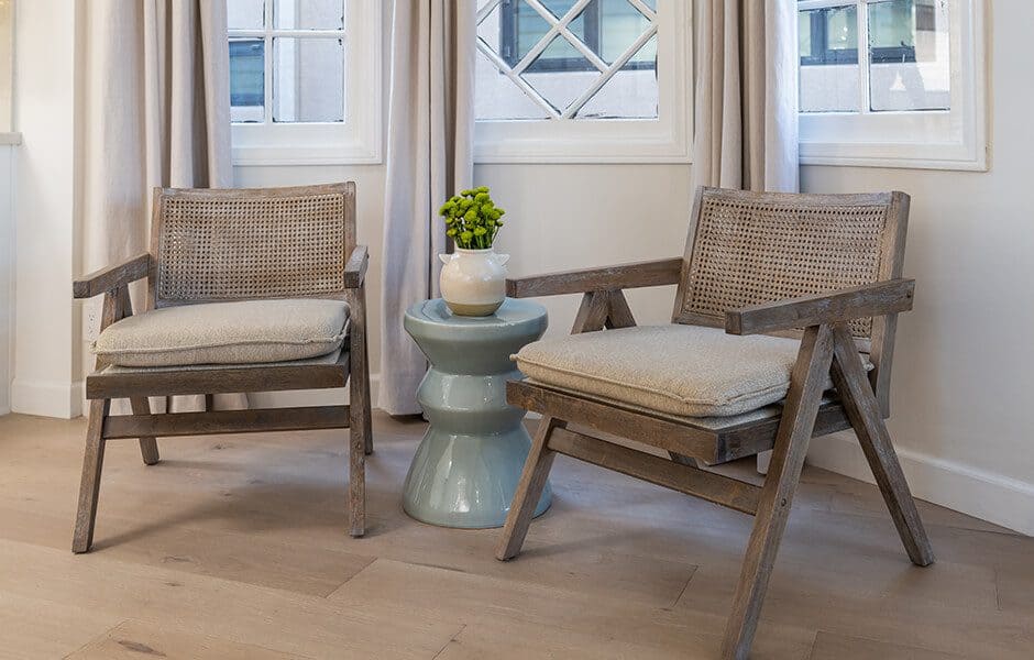 Cozy seating area with wooden cane chairs, cushioned seats, ceramic side table and neutral decor