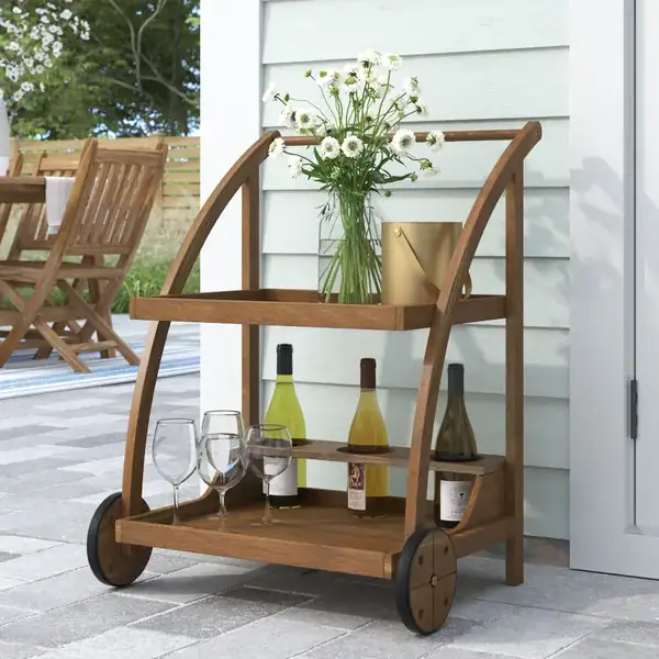 Wooden outdoor bar cart with wine bottles, glasses, and a vase of flowers on a patio