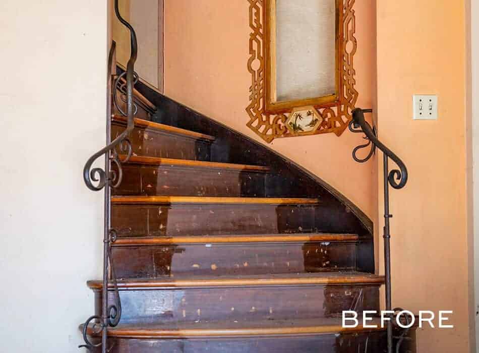 Worn spiral staircase with dark wooden steps, black iron railings, and a decorative mirror on the peach-colored wall