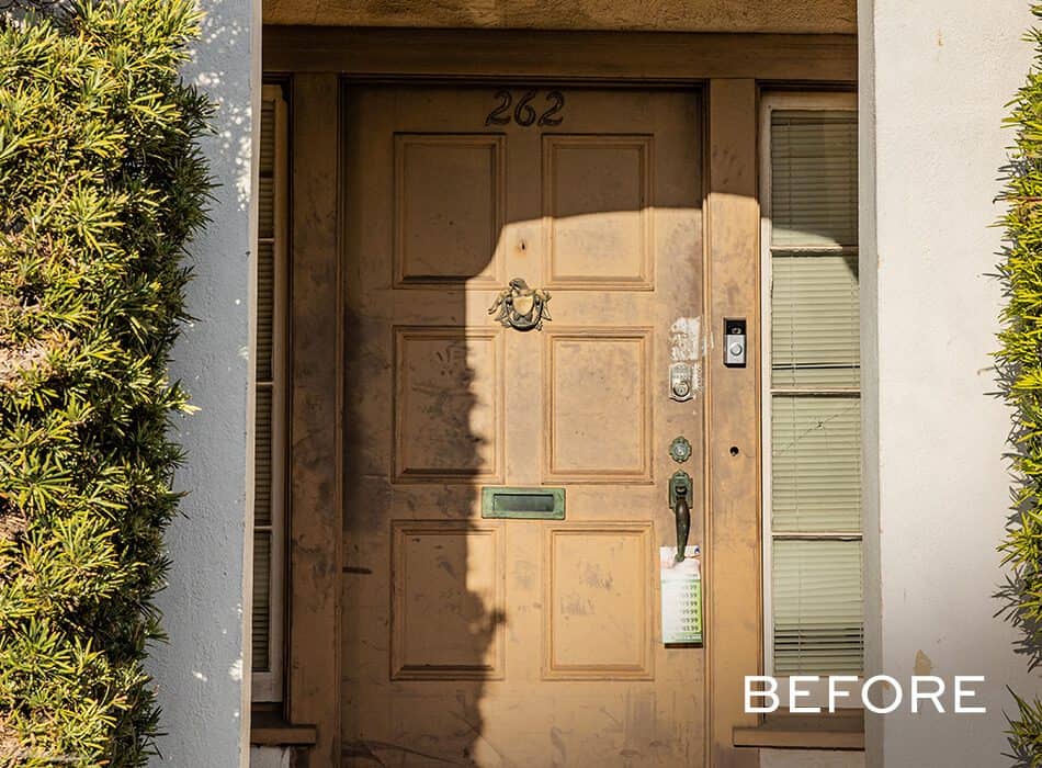 Weathered front door with a brass knocker and flanked by narrow windows, surrounded by greenery
