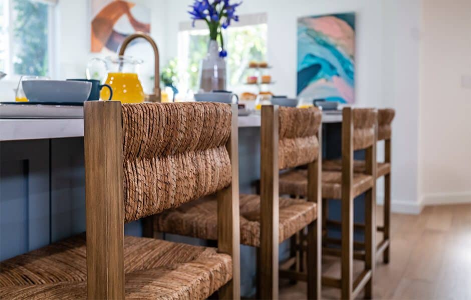 Row of woven rattan bar stools with wooden frames, arranged around a kitchen island