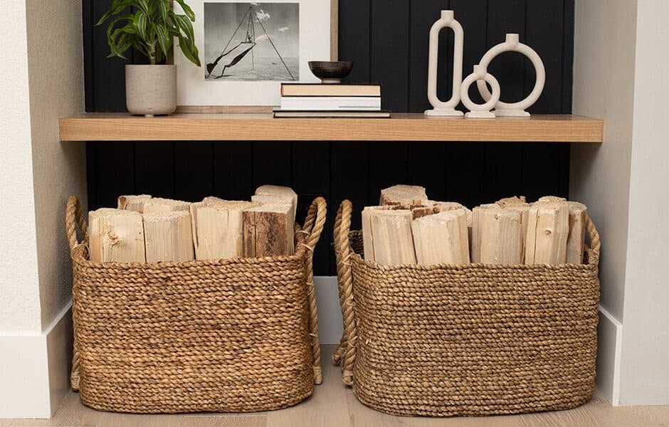 Woven baskets filled with firewood under a wooden shelf with decor