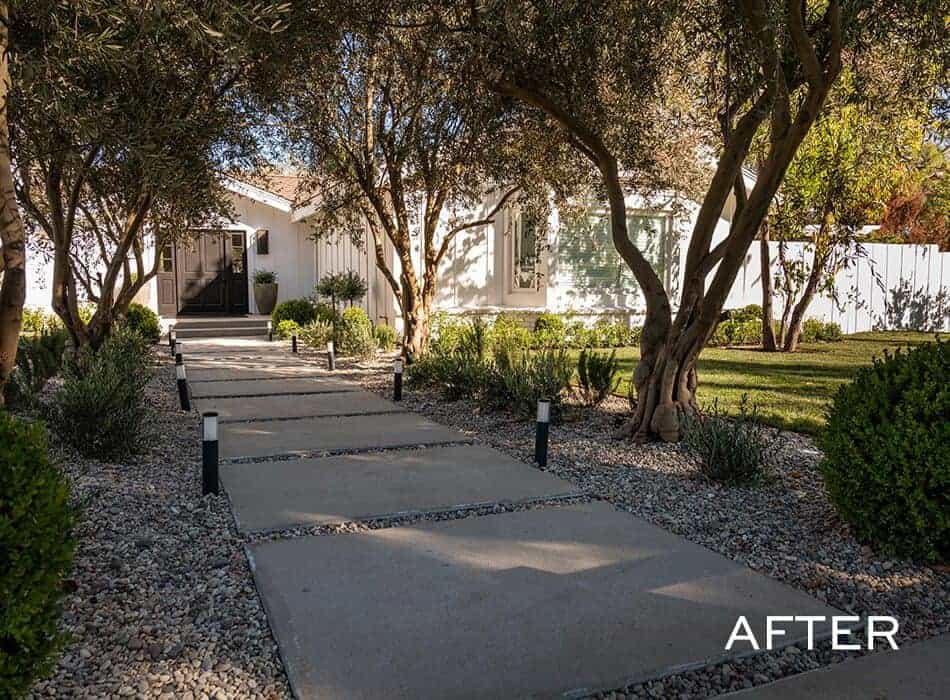 Concrete path with lights, gravel, shrubs, and trees leading to a white house entrance