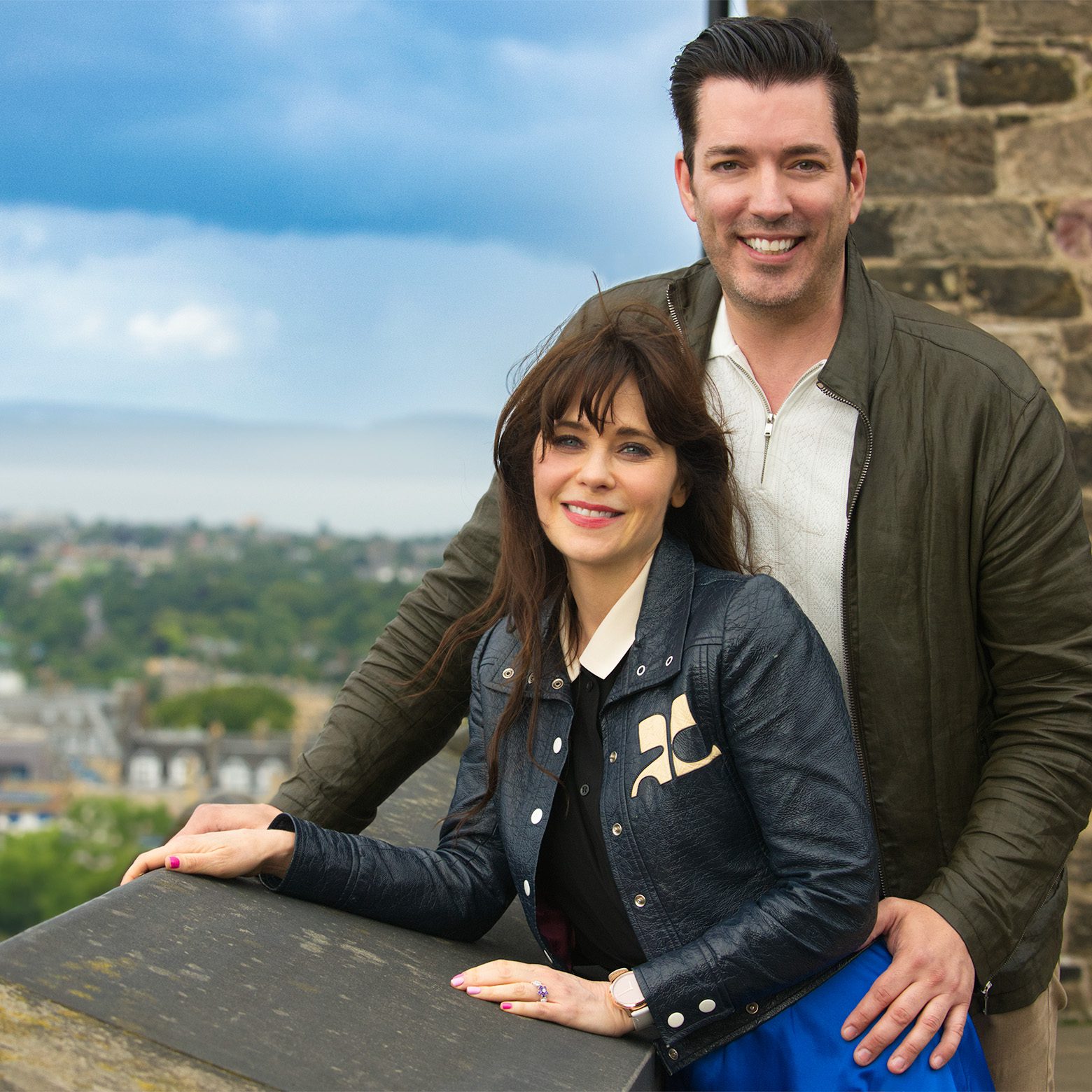 Jonathan and Zooey posing by a stone wall with a scenic view in the background