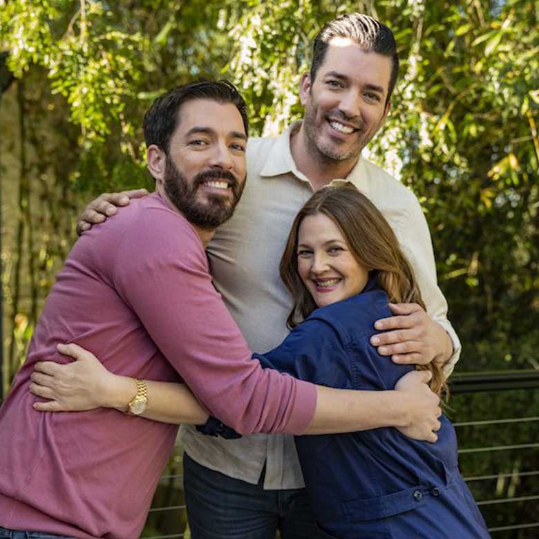 Drew and Jonathan hugging and smiling with Drew Barrymore outdoors with greenery in the background