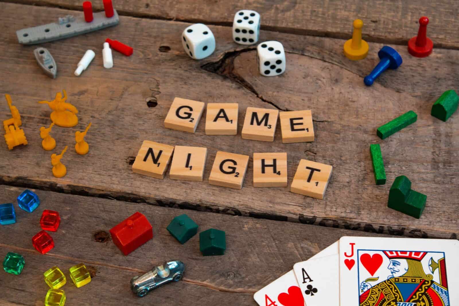 Board game pieces, dice, and cards around wooden tiles spelling “Game Night.”