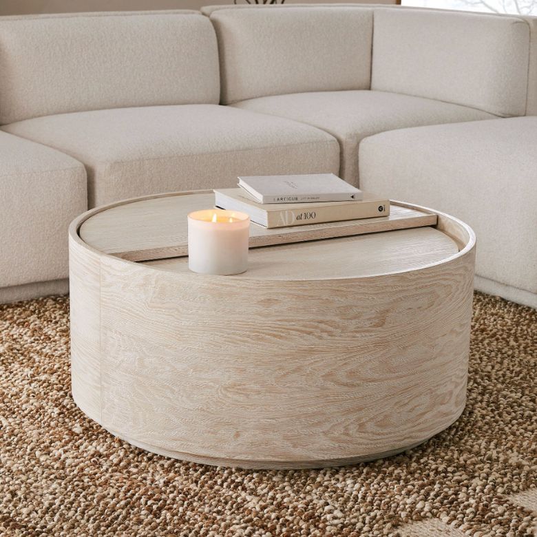Round light wood coffee table with a candle and books on top in a neutral living room