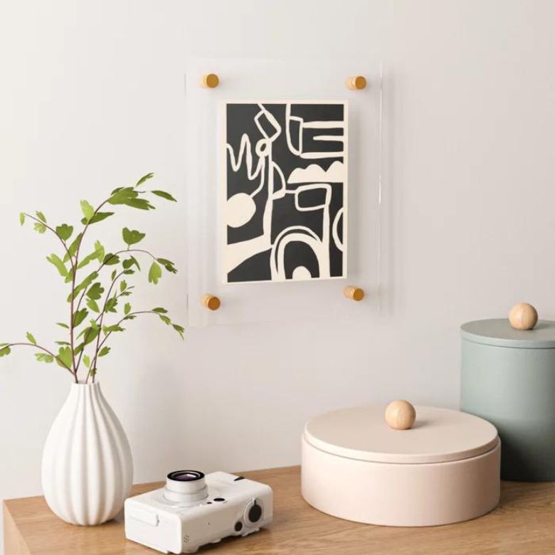 Minimalist decor setup with abstract wall art, potted plant, camera, and round storage boxes on a wooden surface