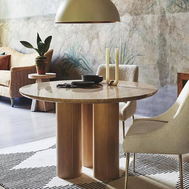 Dining area with a round wooden table, upholstered chairs, modern pendant light, and textured wall mural