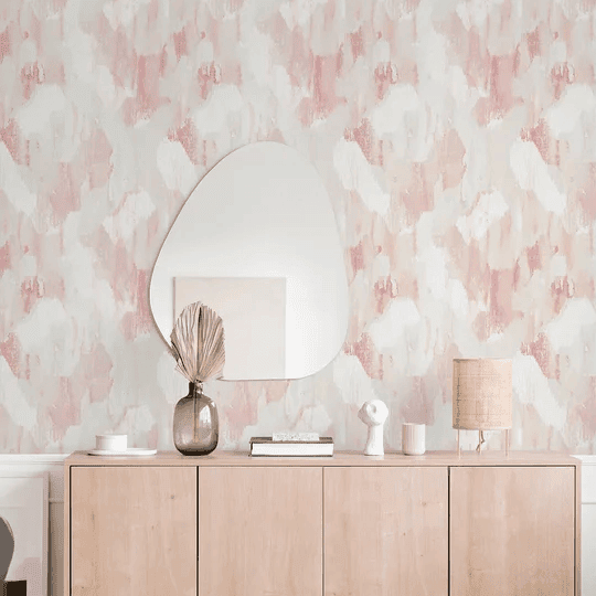 Light wood sideboard with decorative items and an irregular mirror against a pink and white abstract wallpaper