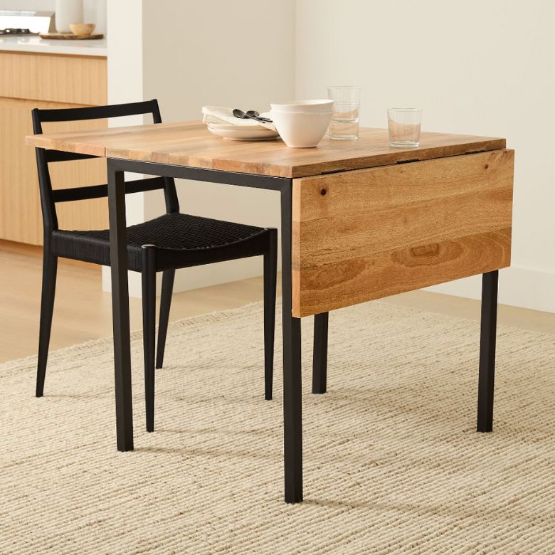 Small wooden drop-leaf table with black metal legs and matching black chair on a beige rug