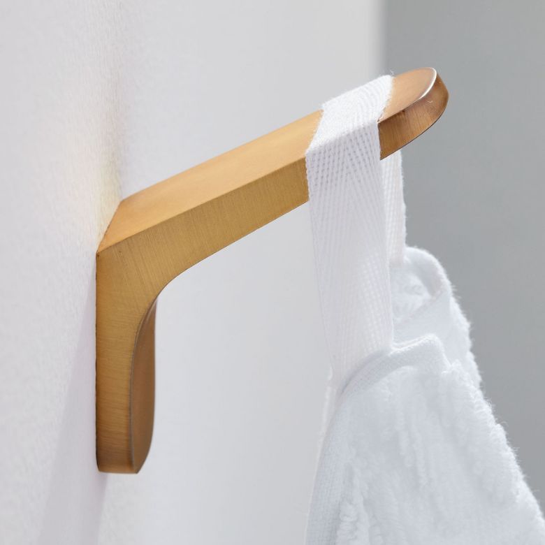 Gold wall hook holding a white towel against a light-colored wall