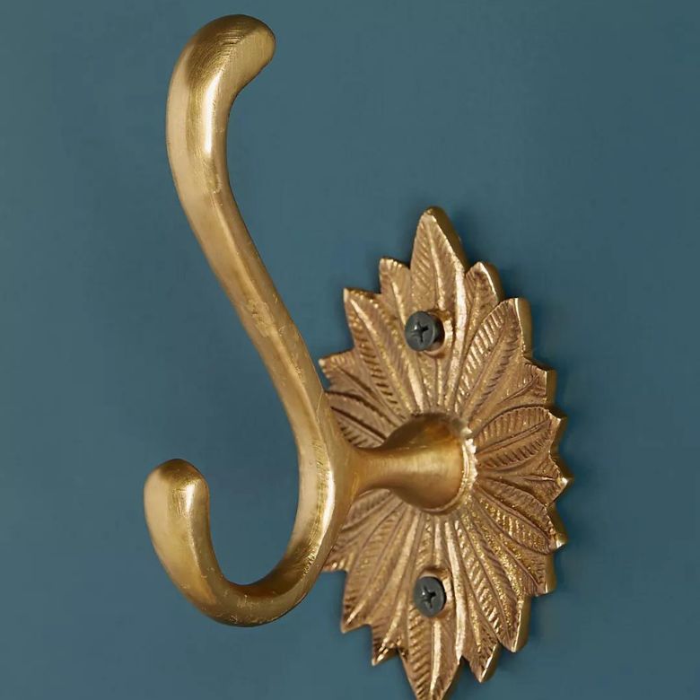 Decorative gold wall hook with a leaf-shaped base mounted on a teal wall