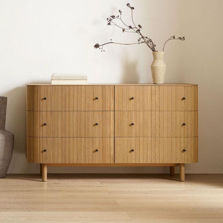 Wooden dresser with vertical grooves and round knobs, topped with a beige vase and minimalist decor