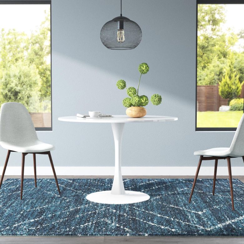 White round pedestal table with two gray chairs on a blue patterned rug, under a black pendant light