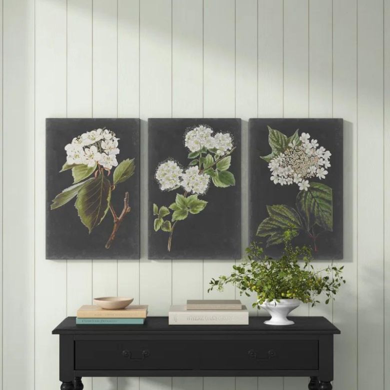 Set of three botanical wall art prints above a black console table with books and a potted plant