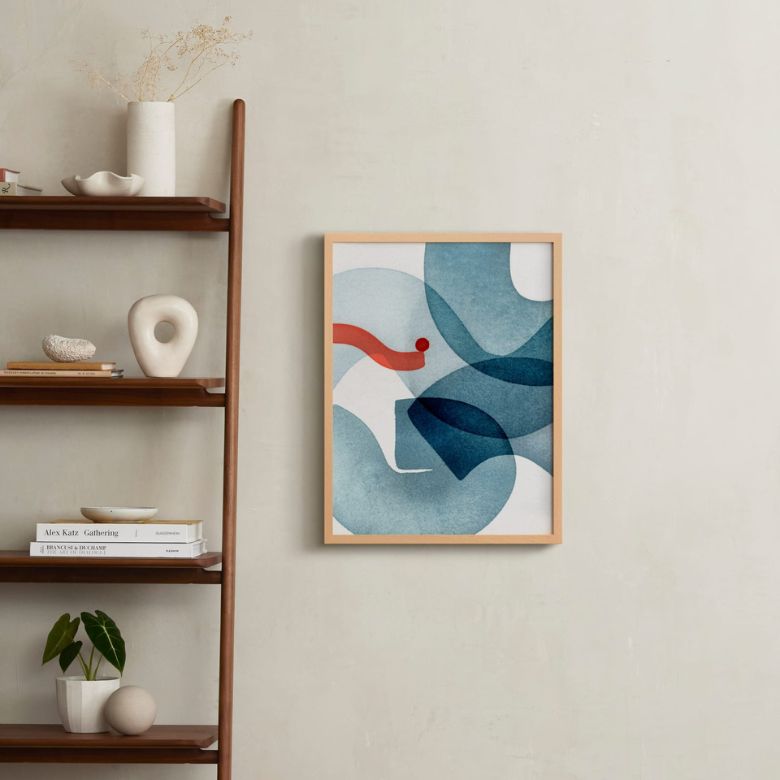 Framed abstract blue and red wall art beside a wooden shelf with minimalist decor and books