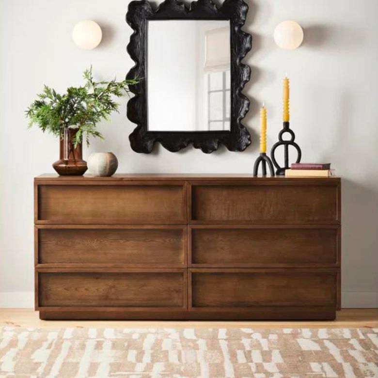 Wooden dresser with six drawers topped with decorative items and a large black-framed mirror