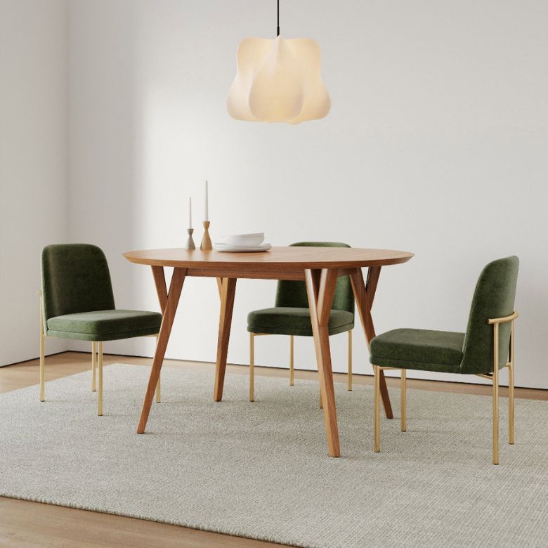 Wood dining table with green velvet chairs and a sculptural pendant light above a neutral rug.