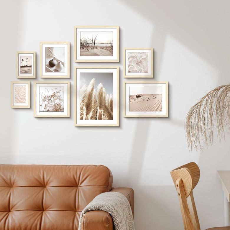 Gallery wall of framed neutral-toned nature prints above a tan leather sofa and wooden chair.