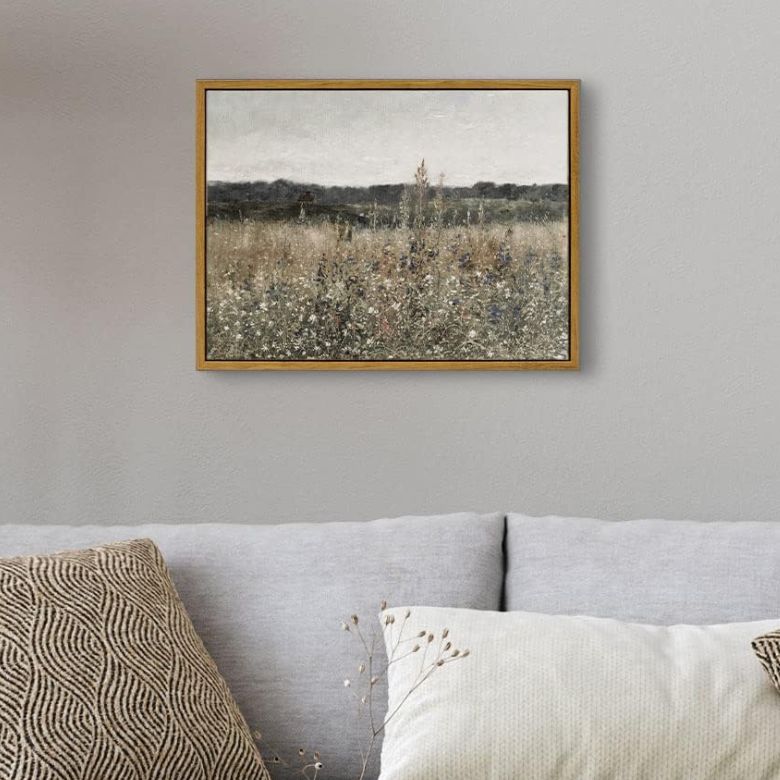 Framed landscape painting of a wildflower field hangs above a light gray sofa with textured pillows.