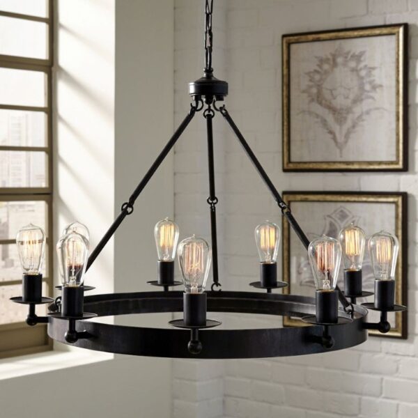 Black metal chandelier with exposed Edison bulbs hangs in a room with framed wall art and large windows.