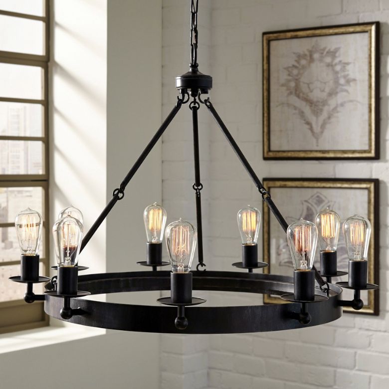 Black metal chandelier with exposed Edison bulbs hangs in a room with framed wall art and large windows.