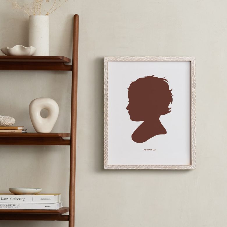 Framed silhouette artwork of a child hangs beside a wooden shelf with minimalist decor pieces.