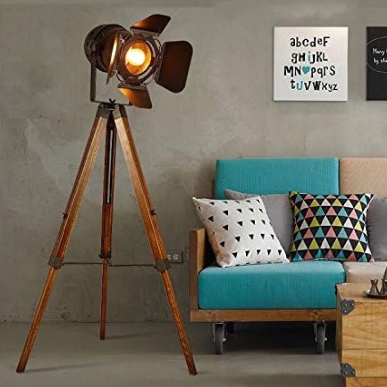 Wooden tripod floor lamp beside blue sofa with patterned pillows.