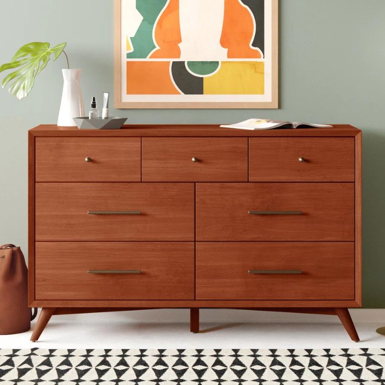 Mid-century wooden dresser with seven drawers beneath a colorful abstract wall art.