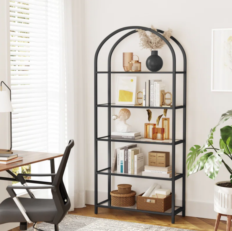 Arched black bookshelf with books, vases, and baskets.