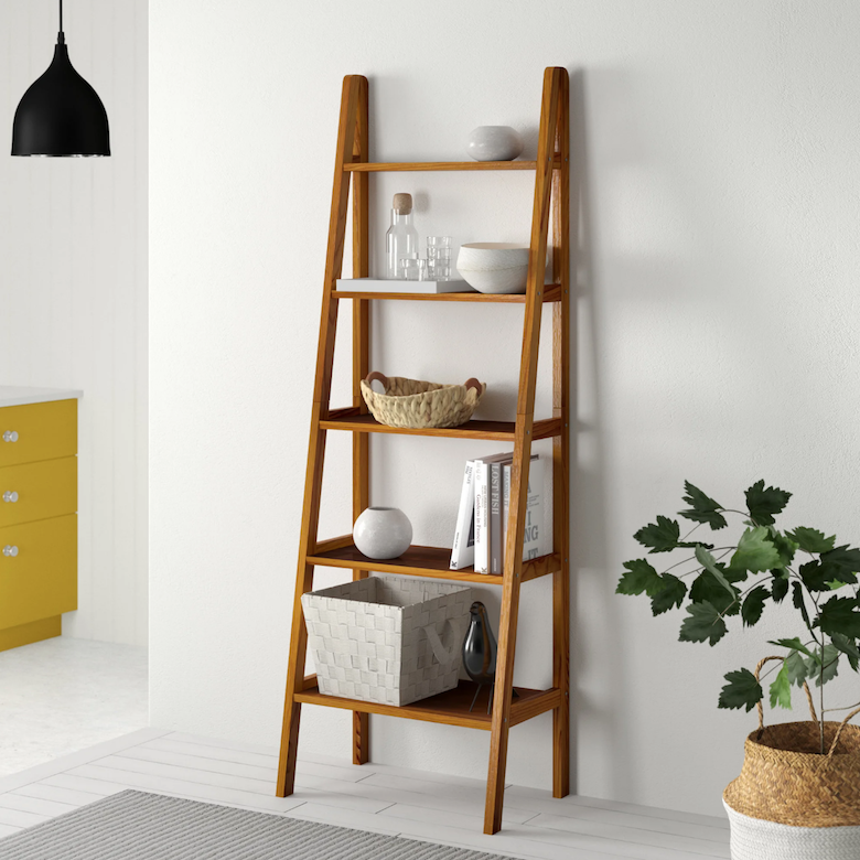 Wooden ladder shelf with bowls, books, and a woven basket beside a potted plant.