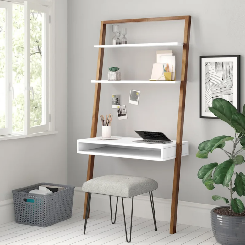 Leaning ladder desk with white shelves, a laptop, and decor paired with a gray stool.