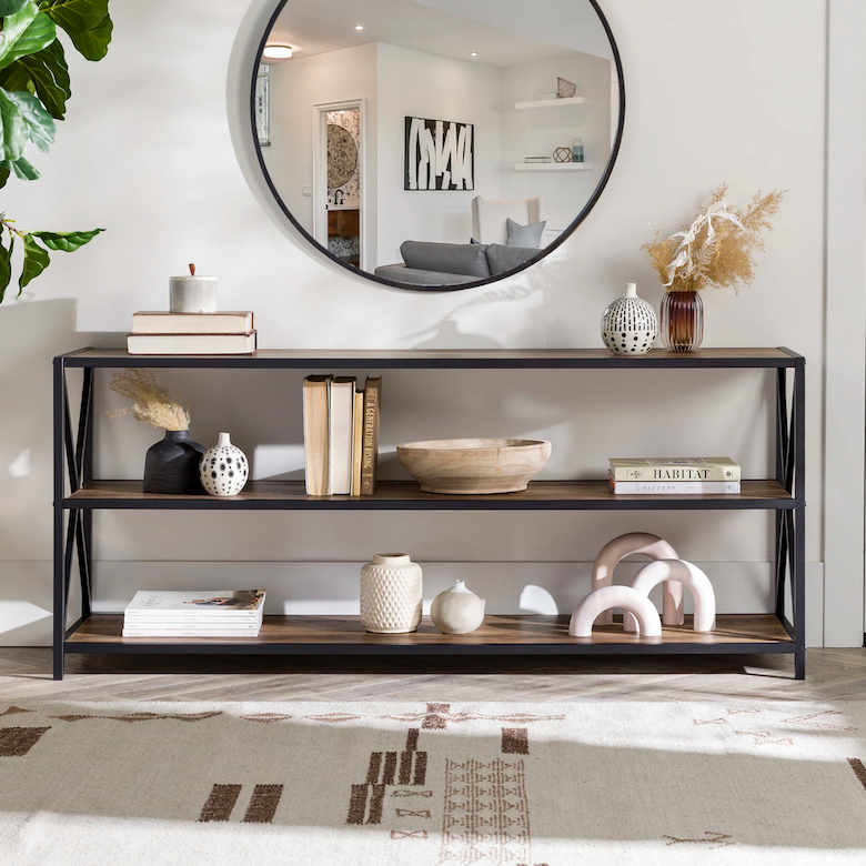 Console table with books, vases, and decor beneath a round wall mirror.