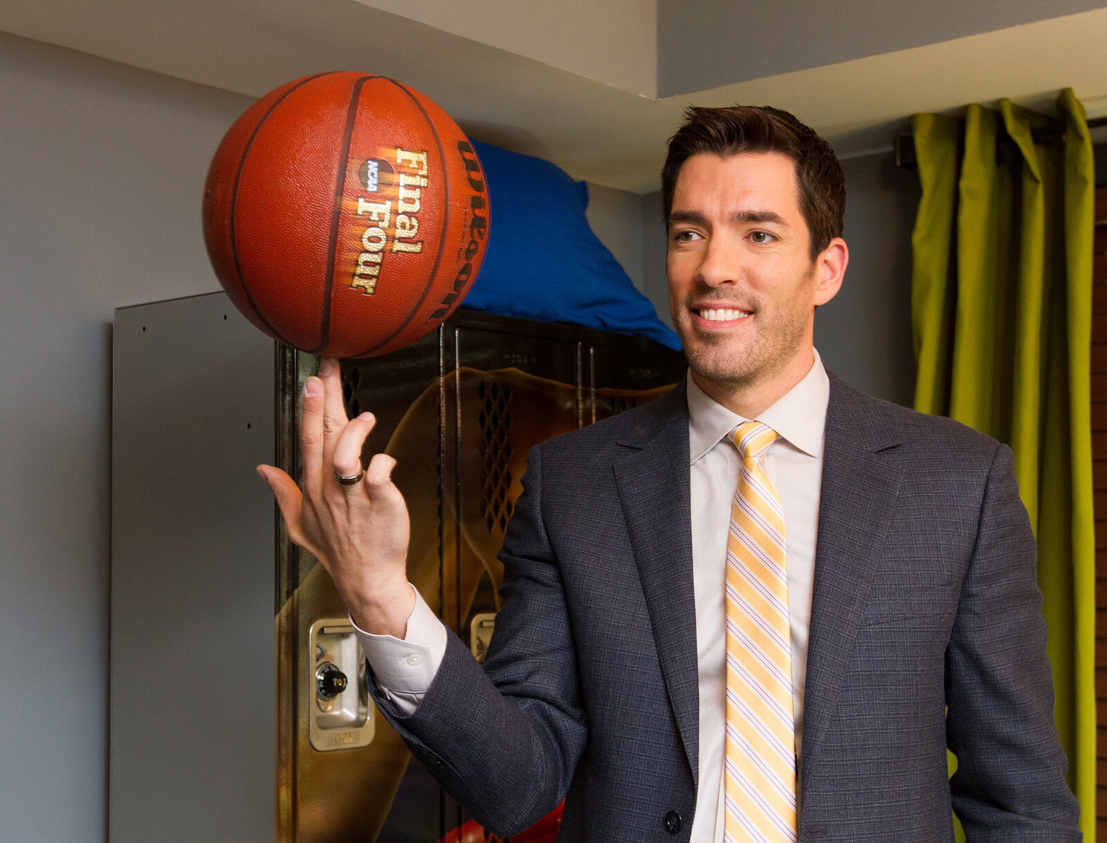 Man in a suit smiling while spinning a basketball on his finger indoors.