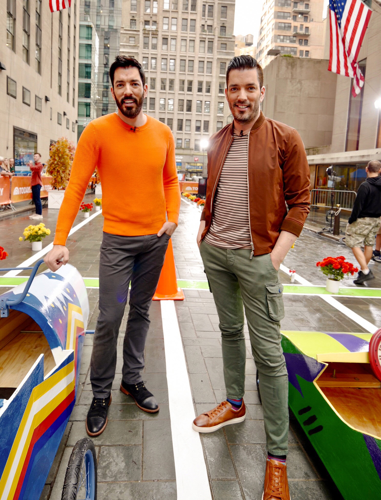 Drew and Jonathan standing outdoors in a city setting beside colorful small race cars.