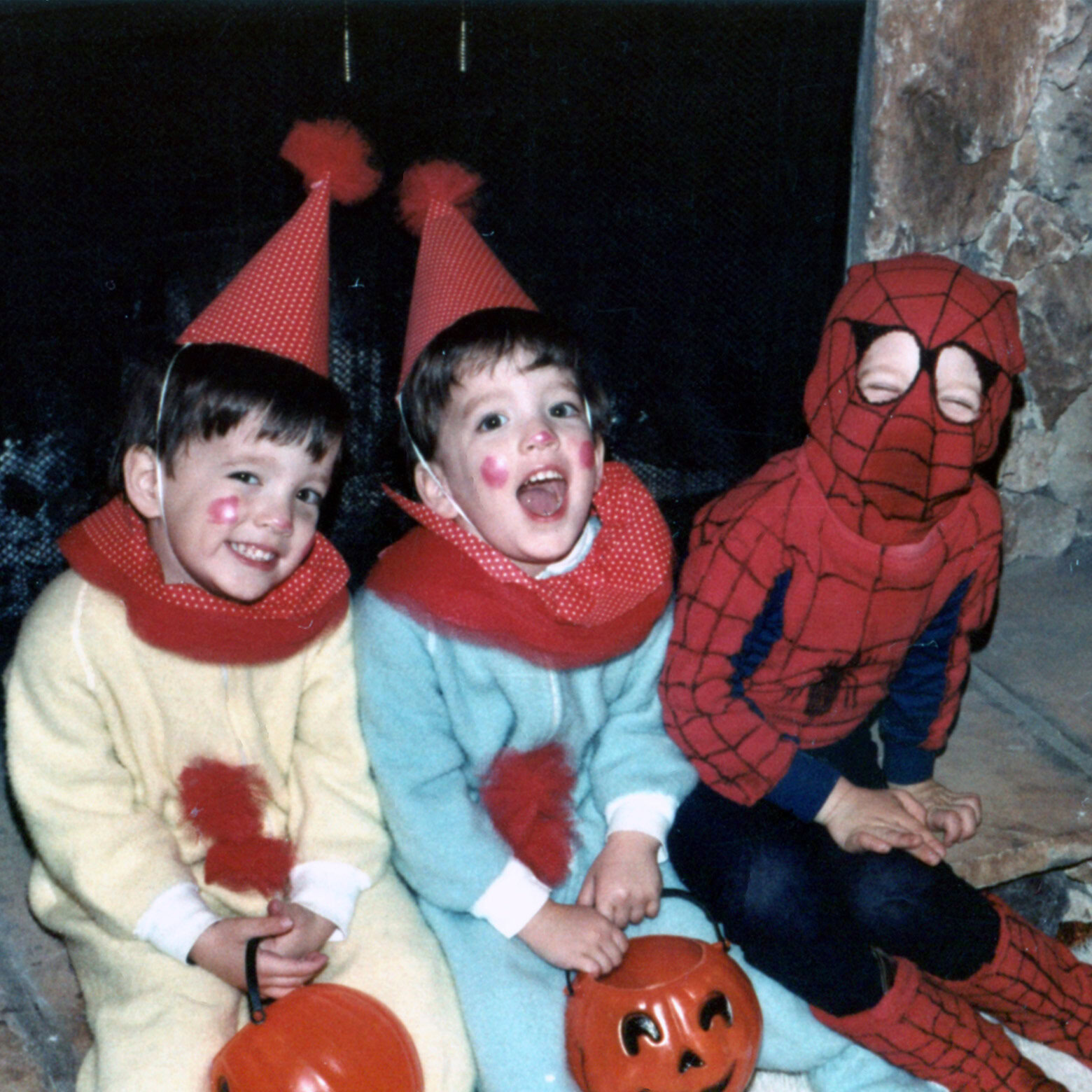 Scott Brothers in Halloween costumes sitting together, two dressed as clowns and one as Spider-Man holding pumpkin buckets.