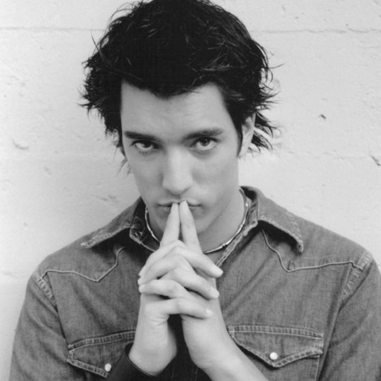 Jonathan in a denim shirt posing with his hands pressed together near his face.