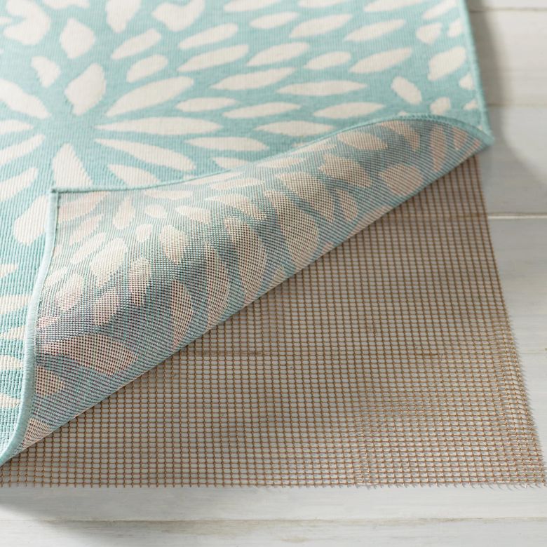 Corner of a patterned rug lifted to show a beige non-slip rug pad underneath.