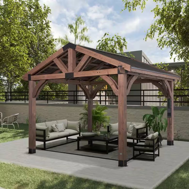 Wooden outdoor gazebo with cushioned seating set on a concrete patio surrounded by greenery.