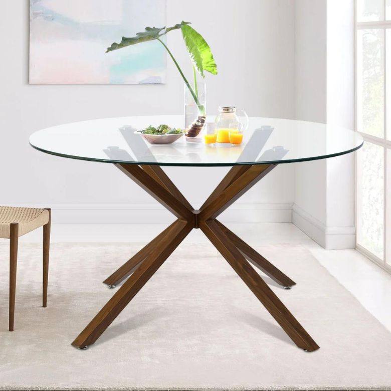 Round glass dining table with crossed wooden legs in a bright, minimal room.