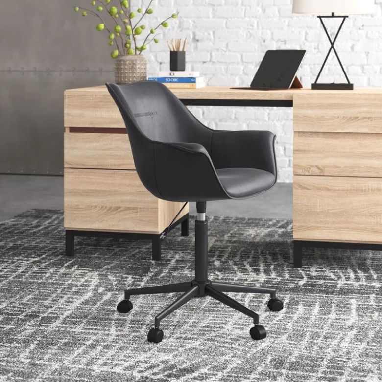 Black swivel office chair with casters in front of a wooden desk and brick wall.