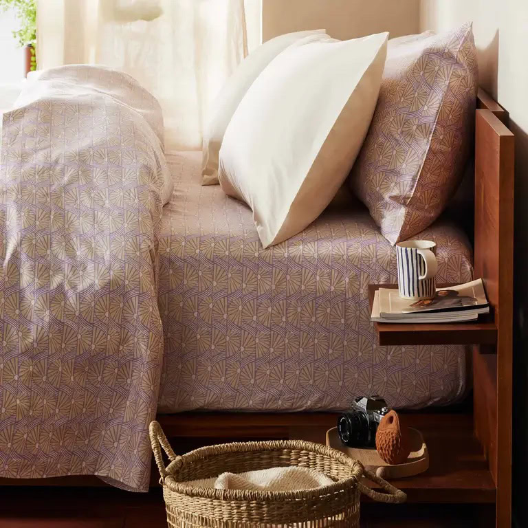 Cozy bedroom with patterned bedding, wooden nightstand, and woven basket on the floor.