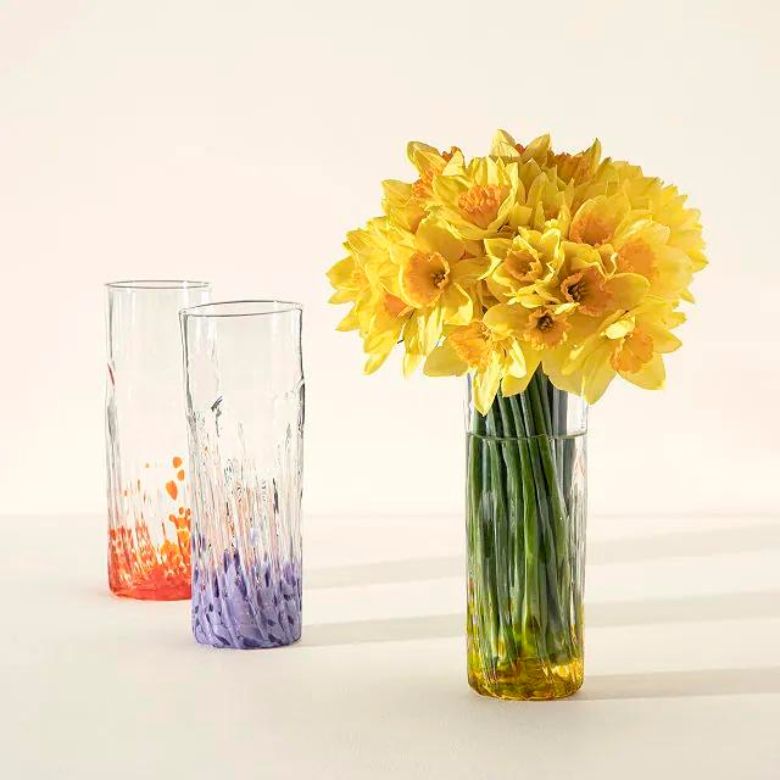 Three tall glass vases with textured designs, one filled with bright yellow daffodils.