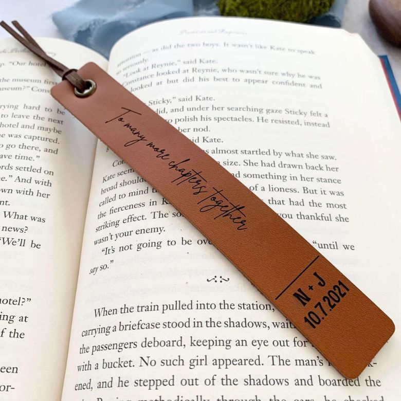 Leather bookmark engraved with a quote resting on an open book.