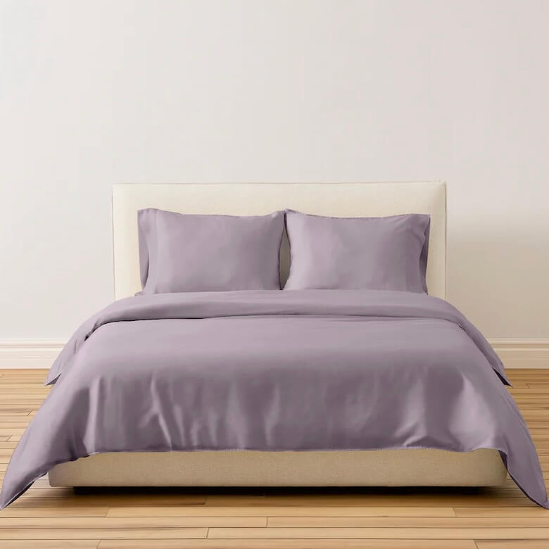Bed with light purple bedding and matching pillows in a simple room.
