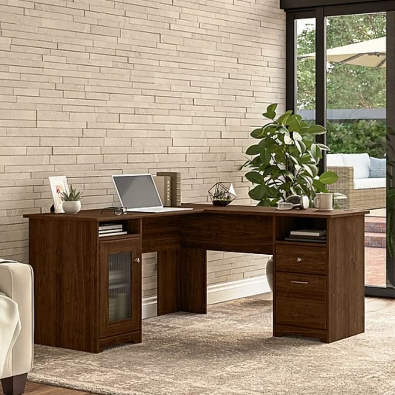 L-shaped wooden desk with a laptop, decor, and storage drawers in a bright home office.