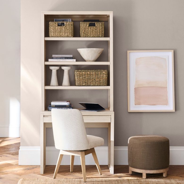 Light wood desk with built-in shelving, woven baskets, and a cream chair in a cozy workspace.