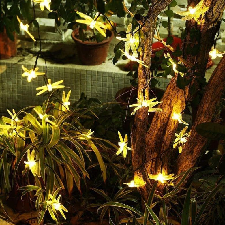Warm yellow string lights shaped like fireflies decorating garden plants and a tree.